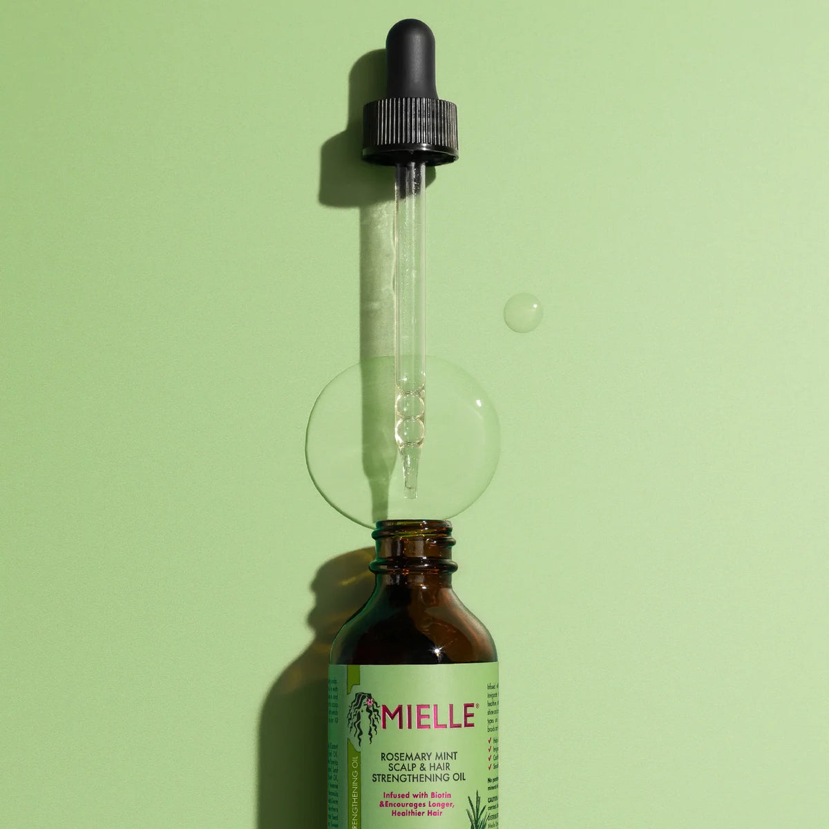 Bottle of Mielle oil with dropper on a green background