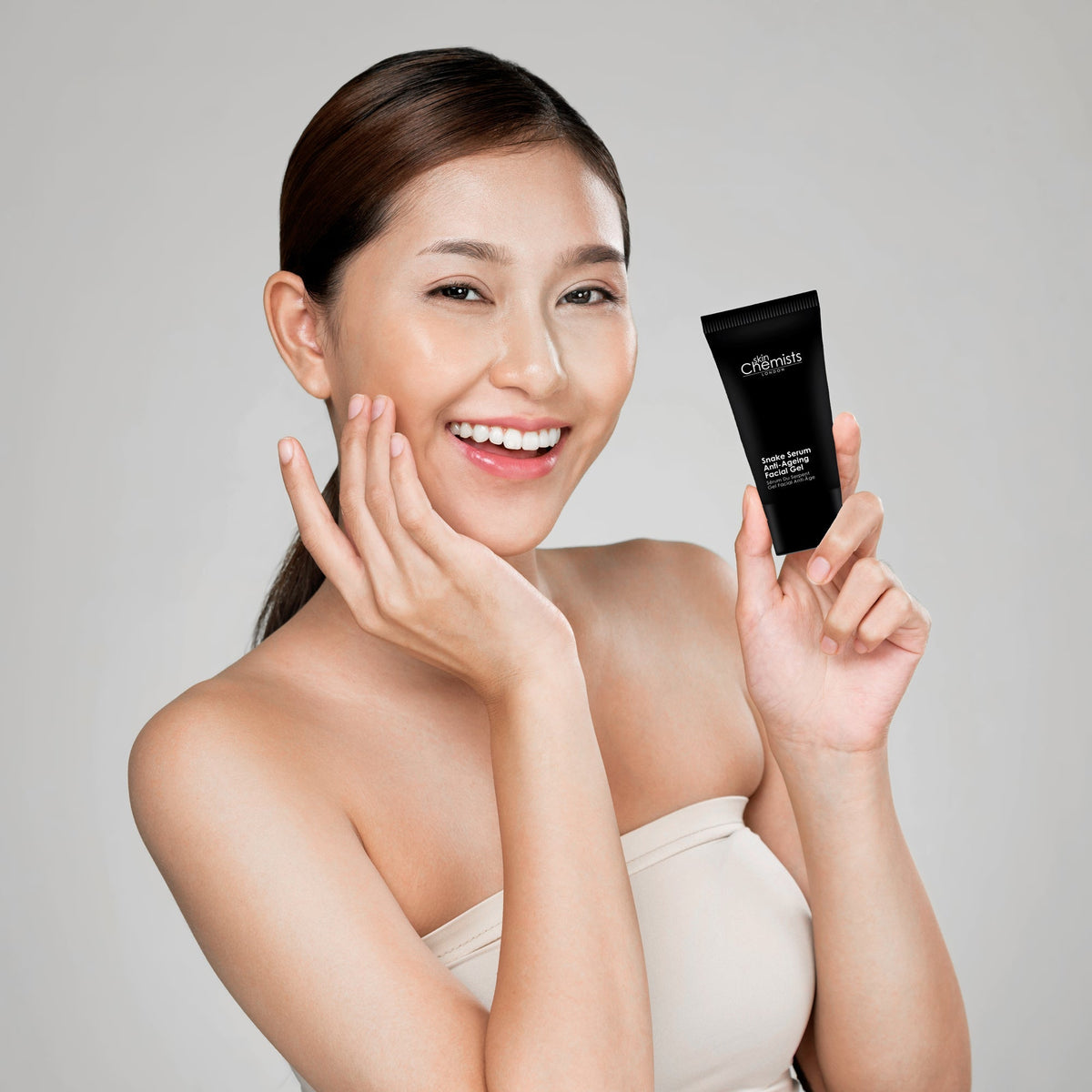 Woman holding a skincare product against a plain background