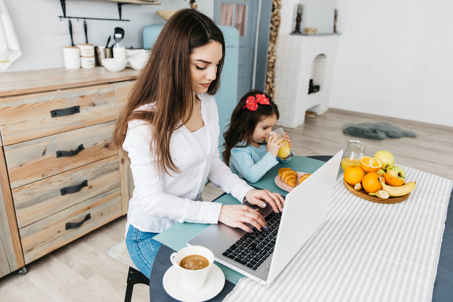 Busy mum working and her daughter drinking juice and eating croissants