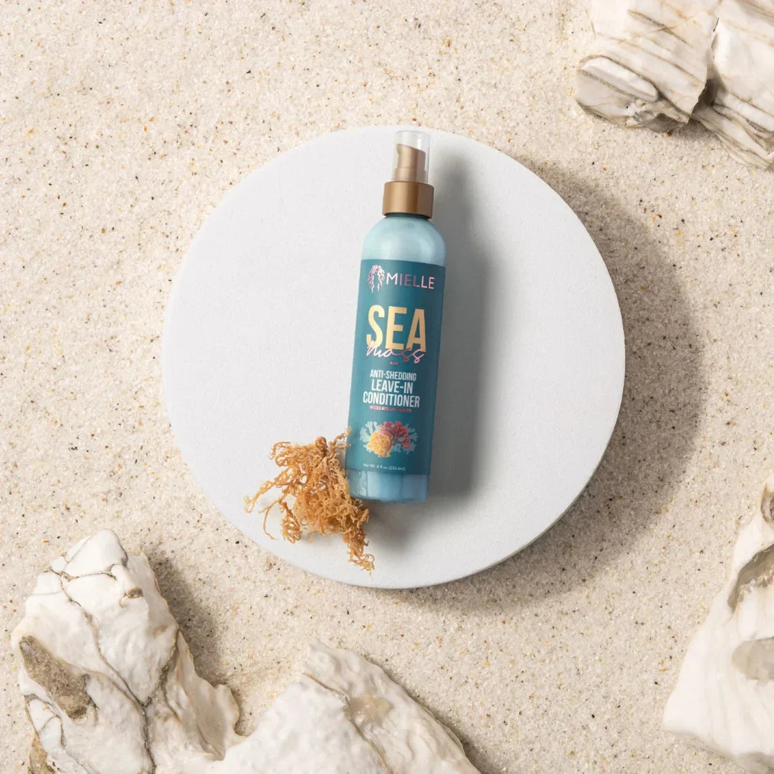 Mielle Sea Moss Leave-In Conditioner placed on a round plate, with sea moss on a sand like effect background