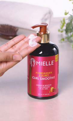 Mielle curl smoothie in a fuchsia pink bottle, hands with with product pumped from the bottle 