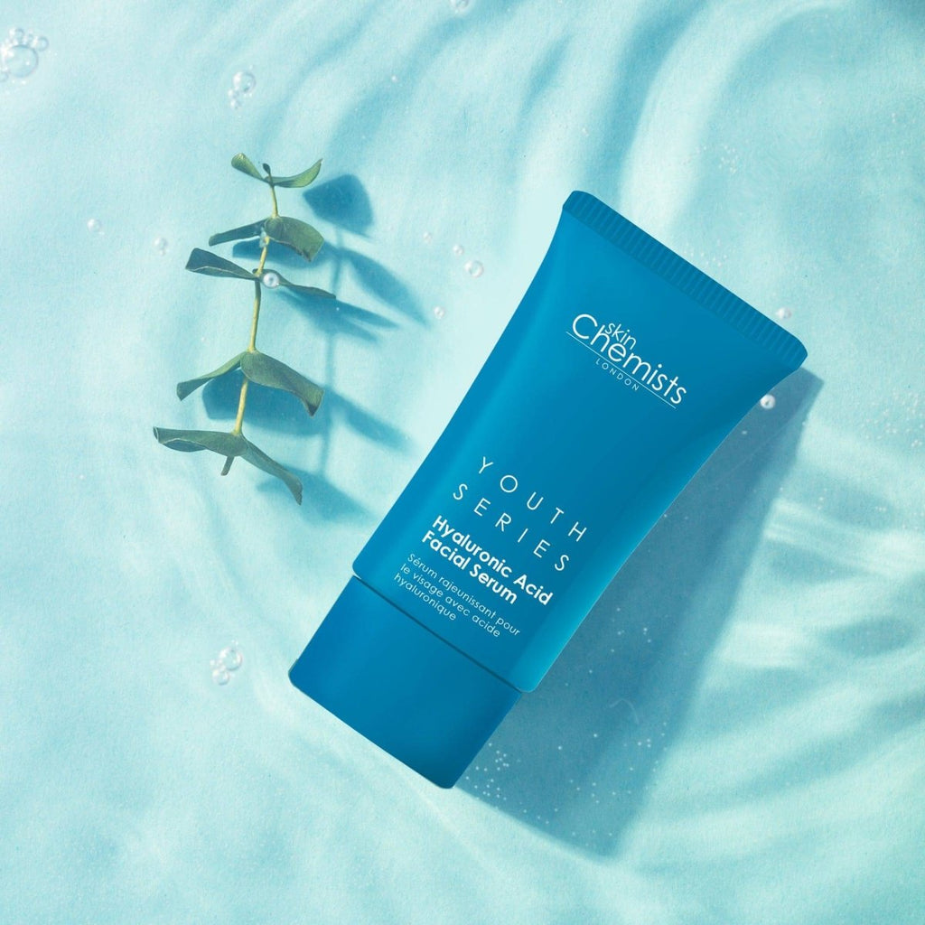 Blue skincare serum tube labeled 'Youth Series' on a light blue background with eucalyptus leaves.