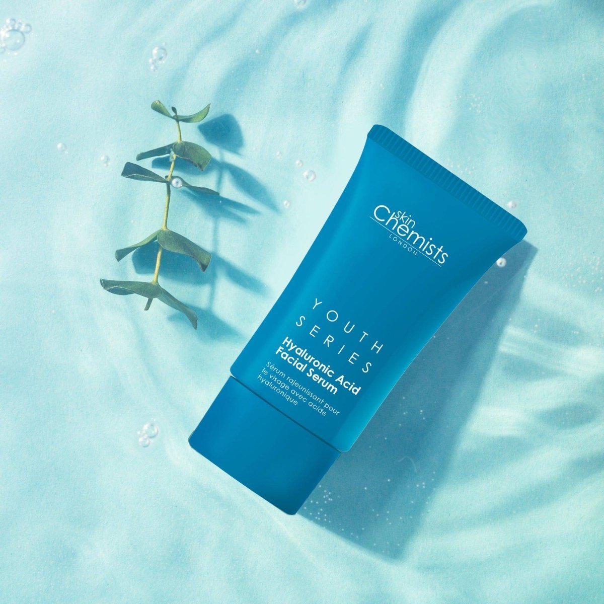 Blue skincare serum tube labeled 'Youth Series' on a light blue background with eucalyptus leaves.