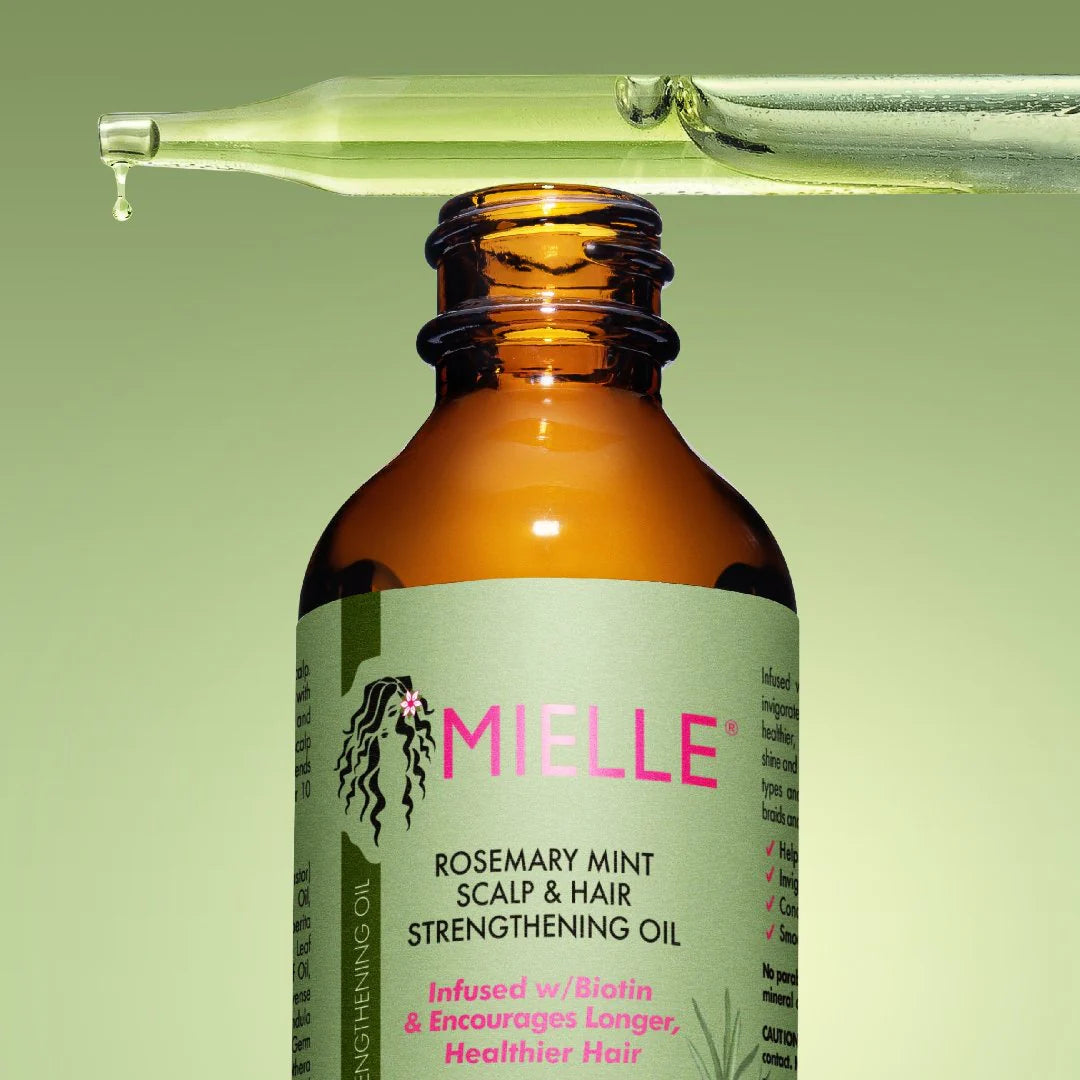 Bottle of MIELLE Rosemary Mint Scalp & Hair Strengthening Oil with a dropper above it on a green background.