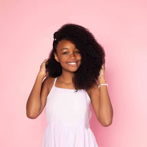 Young woman with curly hair wearing a white dress against a pink background