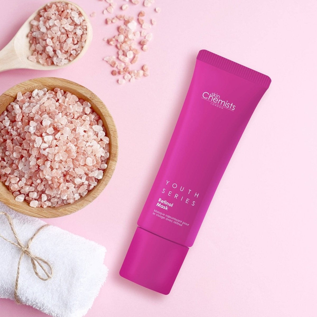 Pink skincare product with 'skin chemists' branding on a pink background with bath salts and towel.