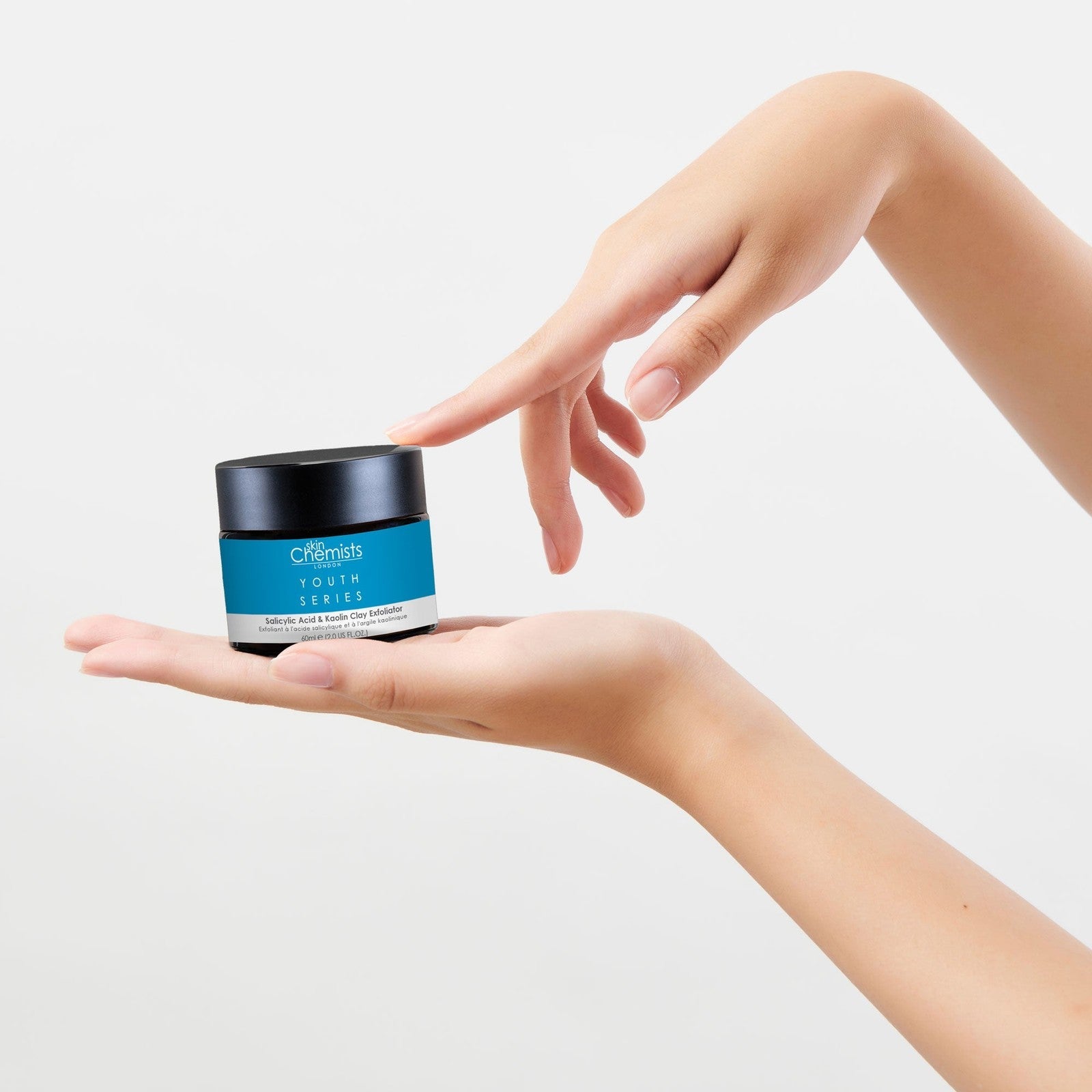 Hand holding a small jar with a blue label against a white background