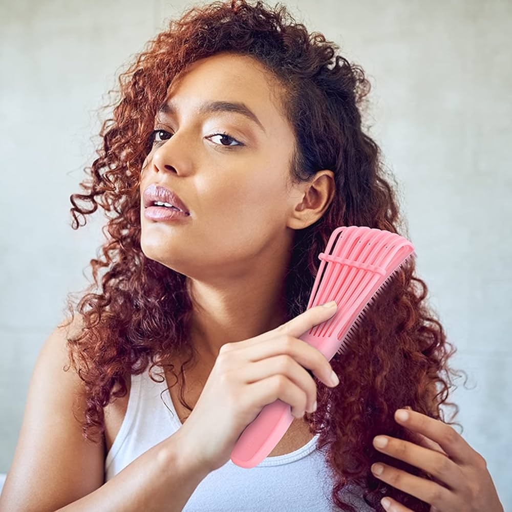 Woman brushing her curly hair with a pink brush against a light background