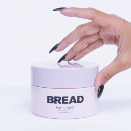 A picture of a woman's hand on top of  a hair cream by the brand Bread