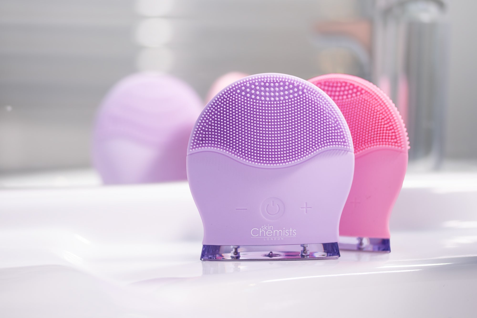 Purple and pink facial cleansing brushes on a white surface with a blurred background