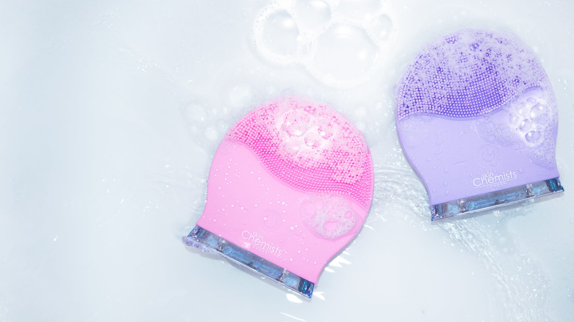 Two silicone caps, one pink and one purple, on a white background with bubbles.