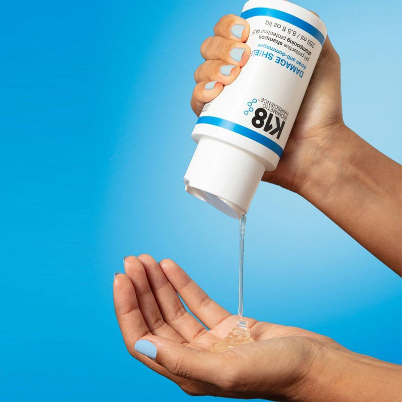 Hand holding a K18 hair product with blue background