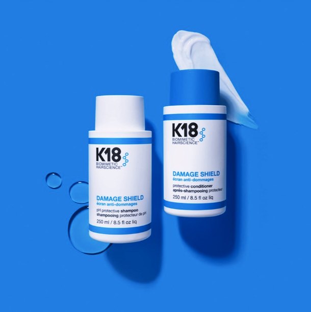 K18 Damage Shield shampoo and conditioner bottles on a blue background