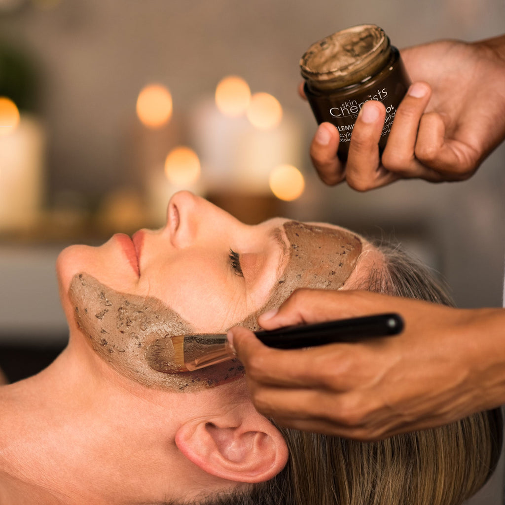 Person applying a hair mask to another person's hair with a jar of product in the background.
