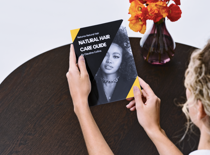 Person holding a 'Natural Hair Care Guide' book on a table with flowers in the background