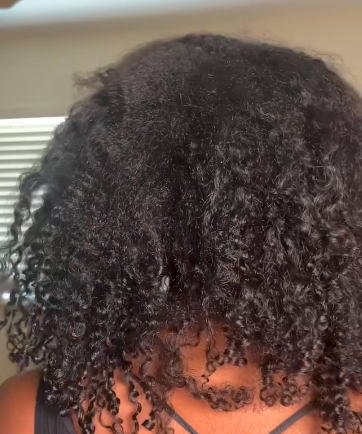 Close-up of a person with curly hair, wearing a black top.