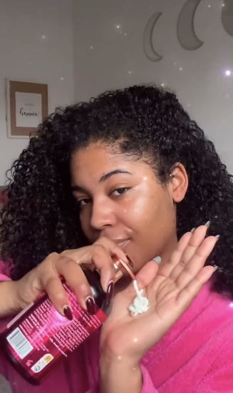 Woman applying a pink lip balm to her lips with a visible brand label.