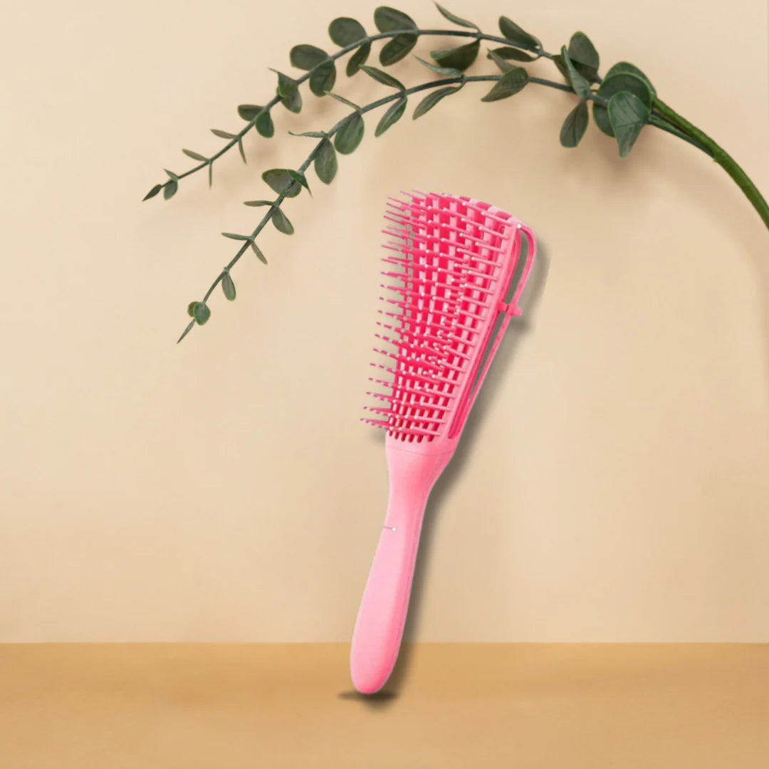 Pink hairbrush on a beige surface with a green leafy branch.
