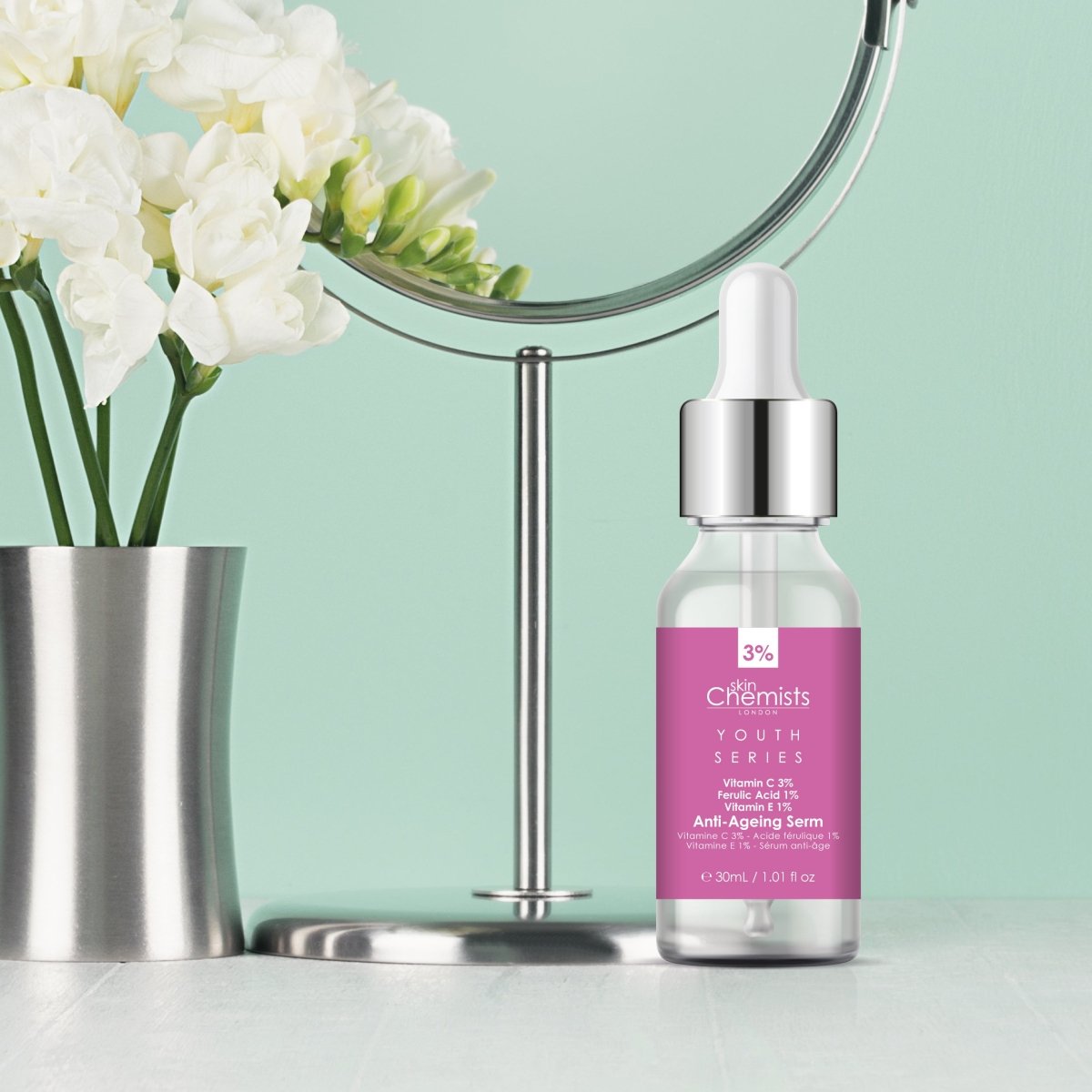 Skincare serum bottle with dropper on a light green background with flowers and a mirror.