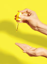 Hand holding a dropper with yellow liquid against a bright yellow background