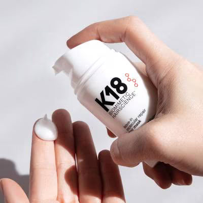 Hand holding a K18 hair mask bottle with a white background
