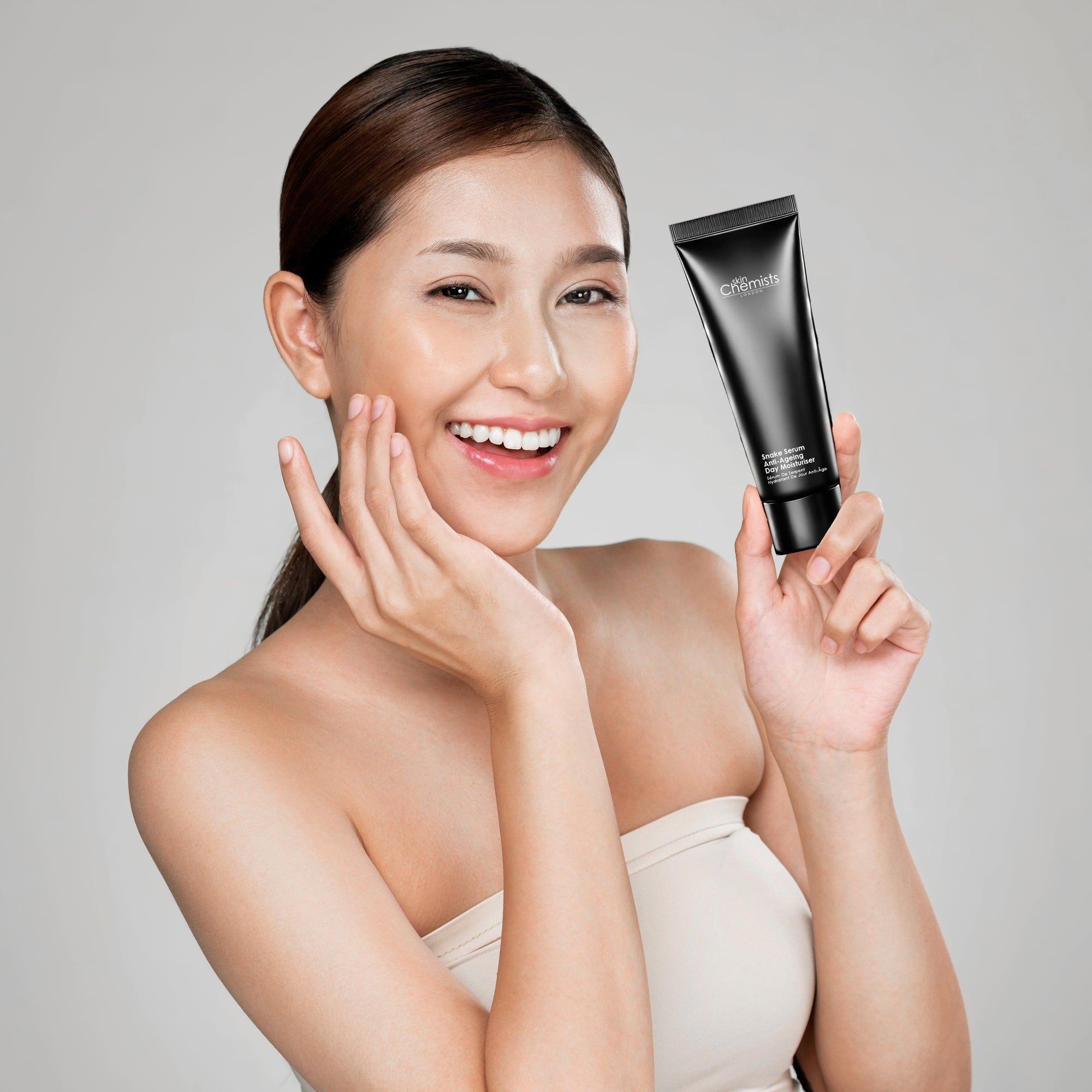 Woman holding a black skincare product against a gray background