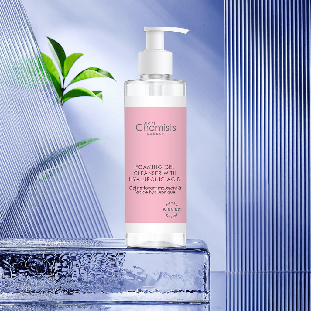 Bottle of 'Skin Chemists' foaming gel cleanser with pink label on a blue and glass background